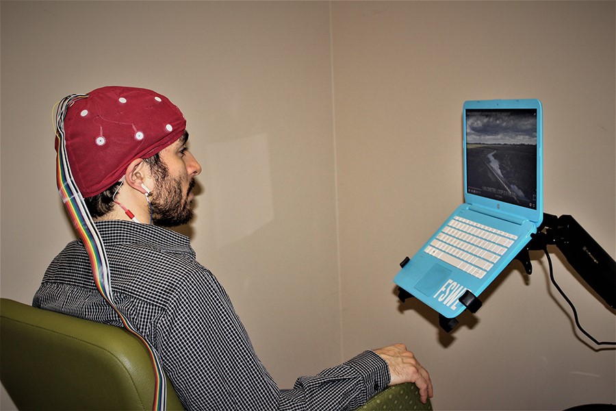 Un jeune homme blanc assis avec un casque de capteurs rouge sur la tête pendant une séance de cartographie cérébrale du service de rétroaction neurologique